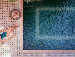 Enjoying suntan. Vacation concept. Top view of young woman near private swimming pool in beautiful moroccan backyard.